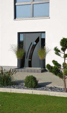 Eleganter Hauseingang mit dunkler Tür und geschwungenem Glaseinsatz, flankiert von hohen Pflanzkübeln und modern gestalteter Vorgartenanlage.