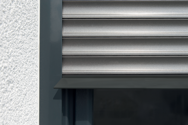 Nahaufnahme eines geschlossenen, silberfarbenen Rollladens an einem modernen Fensterrahmen.