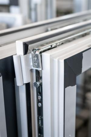Das Bild zeigt eine detailreiche Nahaufnahme eines Fensterbeschlags mit Scharnier, Dichtung und Verriegelungstechnik.