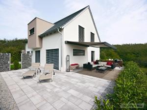 Modernes Flachdachhaus mit großer Glasfront, Außenjalousien und ausfahrbarer Markise auf einer sonnigen Terrasse mit Garten.